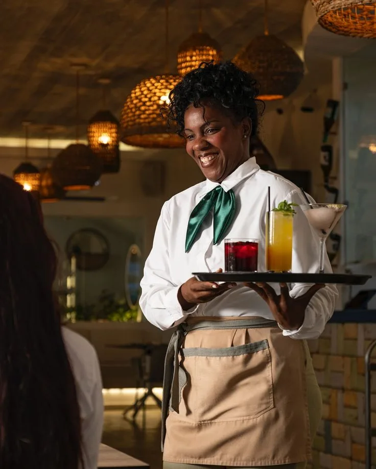 Smiling waitress carrying a tray of colorful drinks through a warm dining room